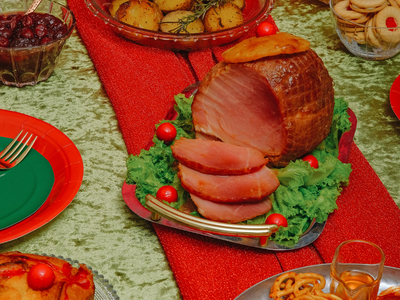 Glazed sliced ham on platter with lettuce and red garnishes on table with side dishes