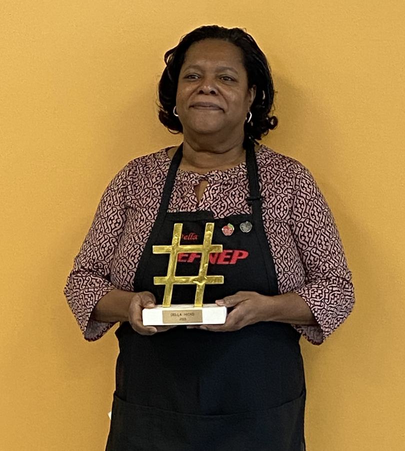 Woman in UTEP apron holding a gold hashtag-shaped trophy on a white base