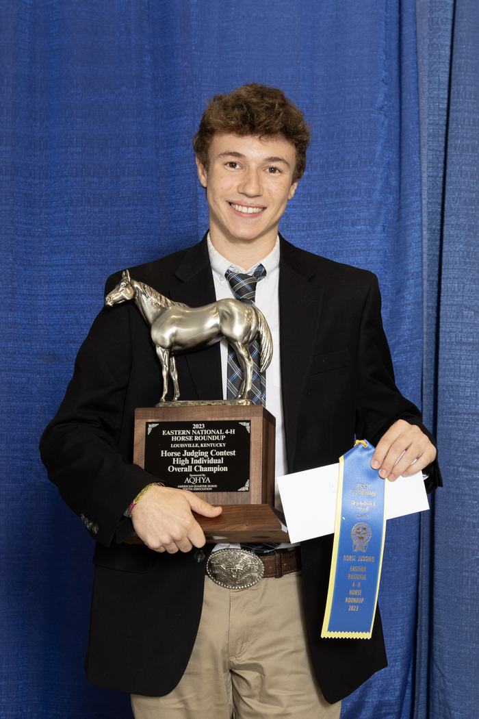 Young man holding horse trophy plaque reading "Overall Champion" and blue "First Premium" ribbon