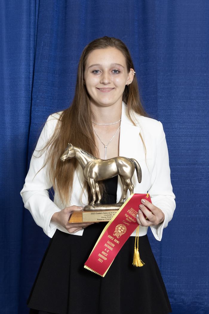Person holding a horse trophy and red ribbon reading "SECOND PREMIUM."