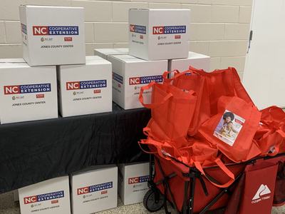 Stacked boxes labeled "NC Cooperative Extension Jones County Center" and red tote bags