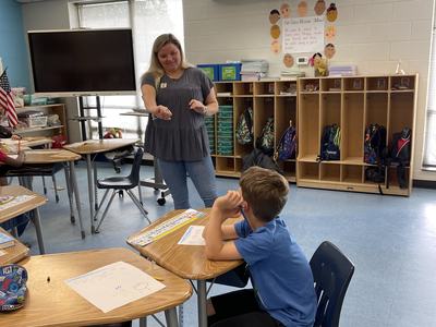 Teacher pointing to a seated student at a desk in an elementary classroom