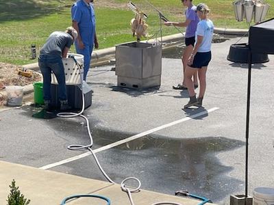Four people standing around an outdoor deep fryer frying turkeys in a parking lot