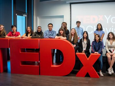 Group of youth posing behind large red TEDx letters with "TEDxYouth" on screen