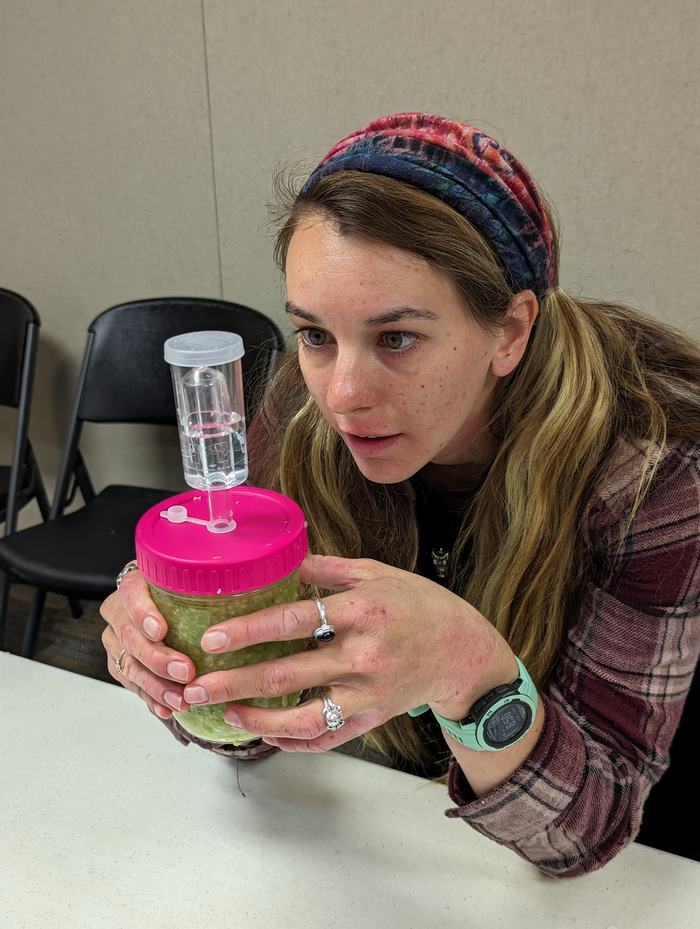 Person holding a jar with pink lid and clear fermentation airlock device attached