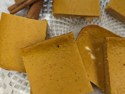 Pumpkin-colored square dessert pieces and cinnamon sticks on a patterned glass plate