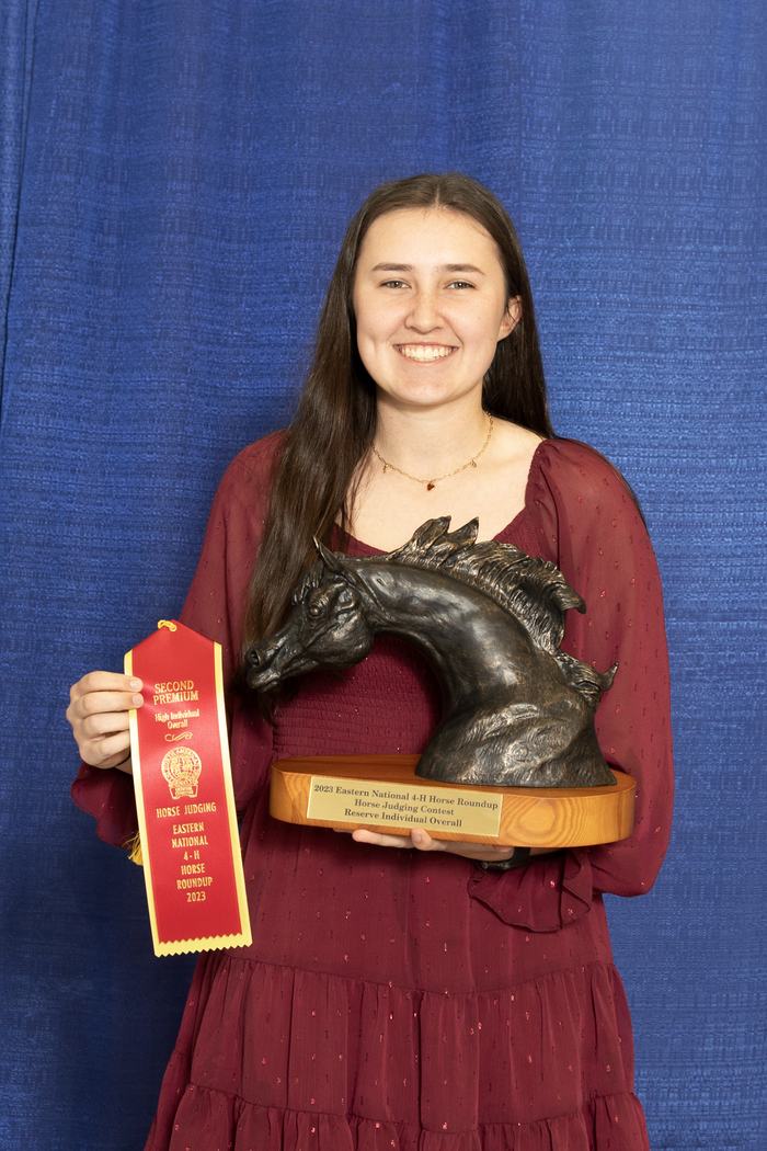 Woman holding horse-head trophy and red ribbon reading "SECOND PREMIUM" "HORSE JUDGING"