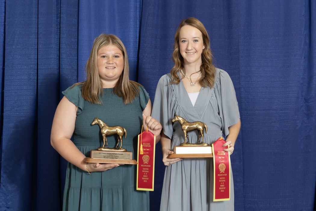 Two young women holding horse trophies and red ribbons reading "SECOND PREMIUM."