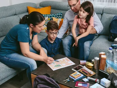 Family gathered on couch pointing at a map with emergency supplies laid out on table