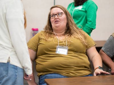 Seated woman at a table wearing glasses and a name badge reading "Abby Whitaker"