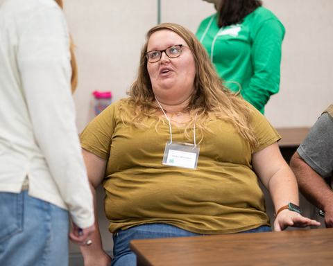 Seated woman at a table wearing glasses and a name badge reading "Abby Whitaker"
