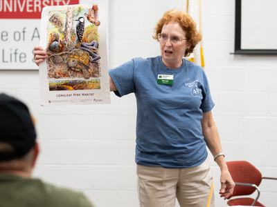 Woman holding poster labeled "LONGLEAF PINE HABITAT" while speaking in a classroom