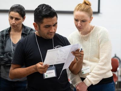 Man and woman reading documents together, visible name tags "Luis Martinez" and "Marianne Martinez"