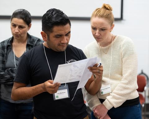 Man and woman reading documents together, visible name tags "Luis Martinez" and "Marianne Martinez"