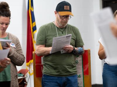 Man in cap and glasses reading a paper labeled "NC State Extension Forestry"