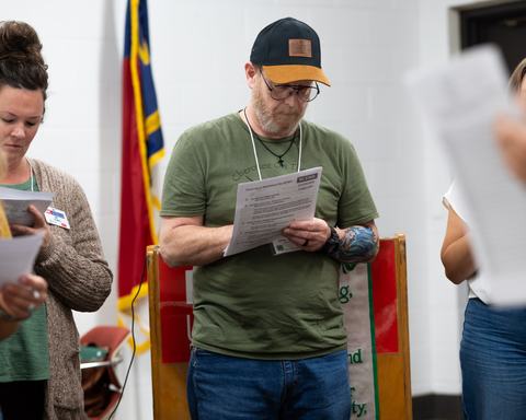 Man in cap and glasses reading a paper labeled "NC State Extension Forestry"