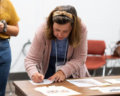 Woman leaning over a table filling out a form with a pen