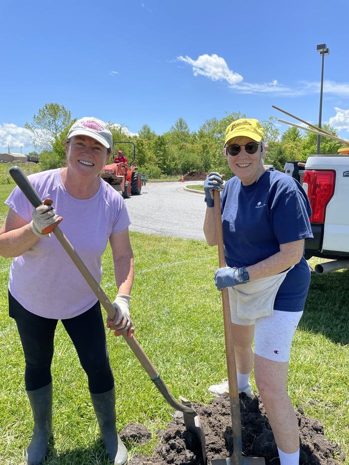 Two women dig a hole together.