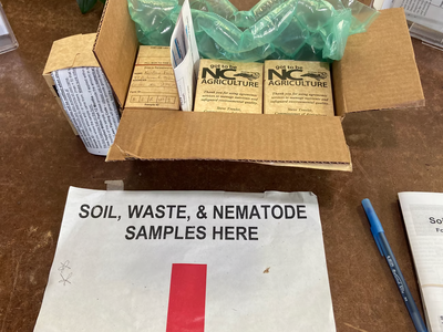 Soil , waste & nematode sample here sign on table with red arrow pointing to drop off location. 4 soil sample boxes in a box.