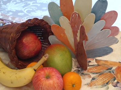 Wicker cornucopia with apples, banana, mango, tangerine and a multicolored wooden turkey decoration