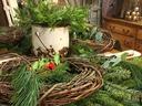 Rusty white metal bucket holding evergreen sprigs surrounded by grapevine wreaths on table