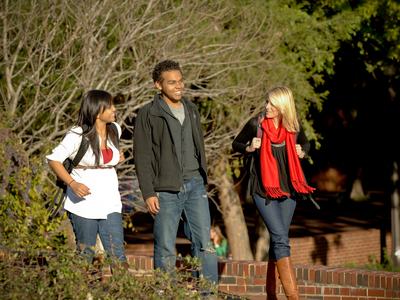 Three students walking on campus with backpacks, one wearing a red scarf