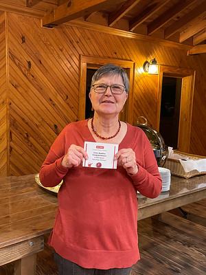 Person in red sweater and glasses holding a small white card in a wood-paneled room