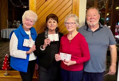 Three older women holding small cards and a man standing beside them at an indoor gathering