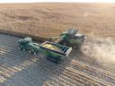 Combine unloading corn into grain cart next to tractor in a harvested cornfield