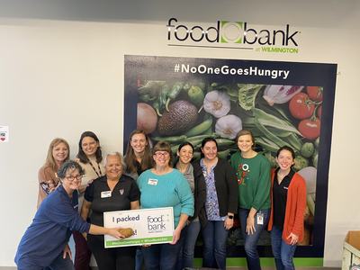 Volunteers holding "I packed" sign at Food Bank at Wilmington backdrop #NoOneGoesHungry