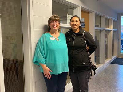 Two women standing in a hallway under sign "COUNTY COMMISSIONERS CHAMBER"
