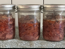 Seven sealed mason jars with canned shredded meat lined on a towel