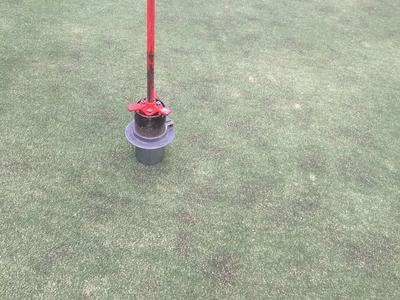 Red turf coring tool standing upright on green turf surface