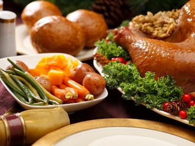 Roasted turkey with stuffing on platter, dinner rolls and bowl of green beans, carrots, potatoes
