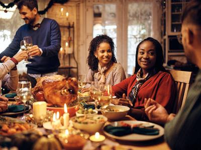 Happy African American woman and her friends communicating while celebrating Thanksgiving at dining table.