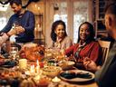 Happy African American woman and her friends communicating while celebrating Thanksgiving at dining table.
