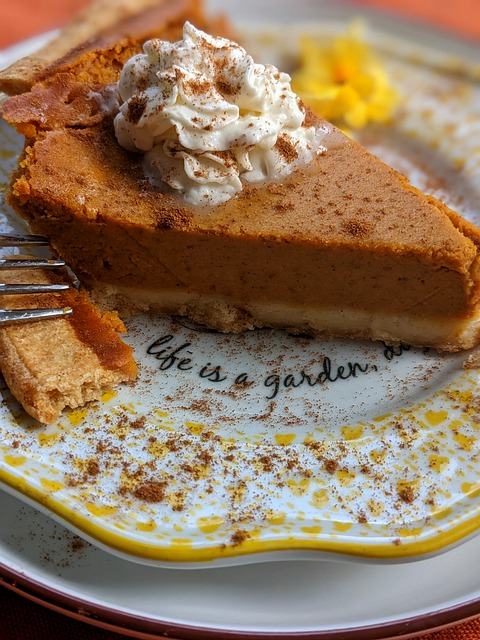 Pumpkin pie with a scoop of whipped cream on top, placed on a plate.