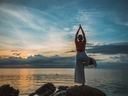 person stretching in a yoga form on a rock in front of the ocean.
