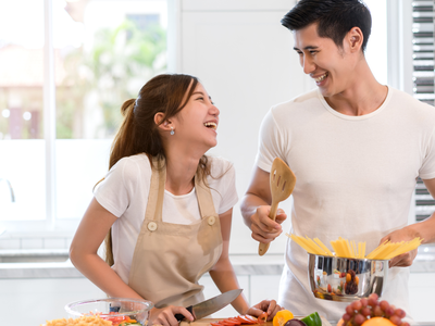 Couple cooking; man with spaghetti pot, woman chopping vegetables. "Happy Valentine's Day"