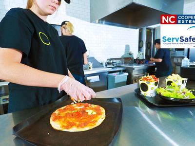 Gloved worker preparing pizza in a commercial kitchen; NC Cooperative Extension ServSafe logo
