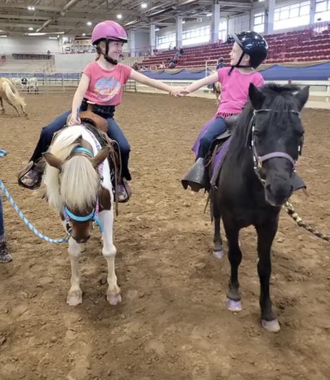 2 young 4-H club friends riding their ponies and holding hands