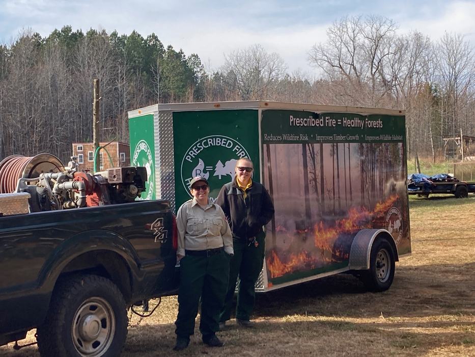 Two people stand in front of a Prescribed Fire trailer.