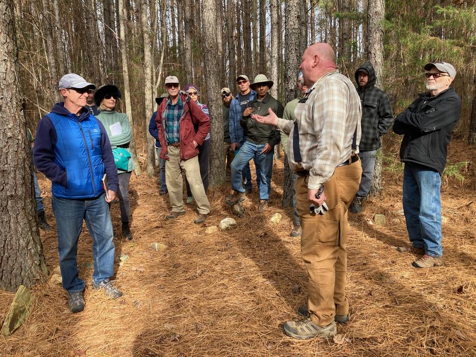 A man teaches a group in a forest.