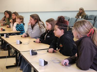 Students seated at tables holding handheld buzzer buttons, facing forward