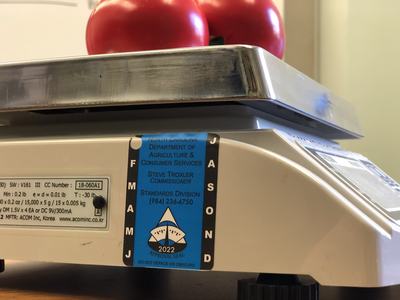 Scale with two tomatoes on metal tray and blue North Carolina approval sticker