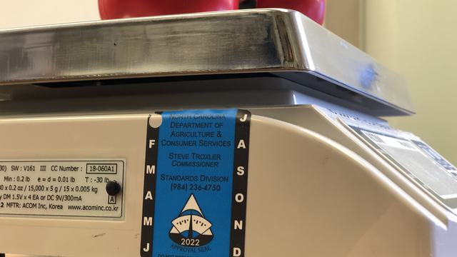 Scale with two tomatoes on metal tray and blue North Carolina approval sticker