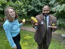 Two people in a garden holding halved yellow fruit; man offers a spoon and fruit half.