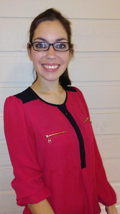 Smiling woman with glasses wearing a red blouse, standing against white horizontal siding