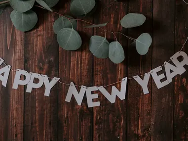 White "HAPPY NEW YEAR" paper banner hanging on string against dark wooden background with eucalyptus leaves