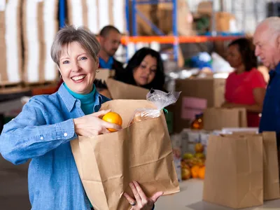 Woman placing an orange into a paper grocery bag at a food pantry